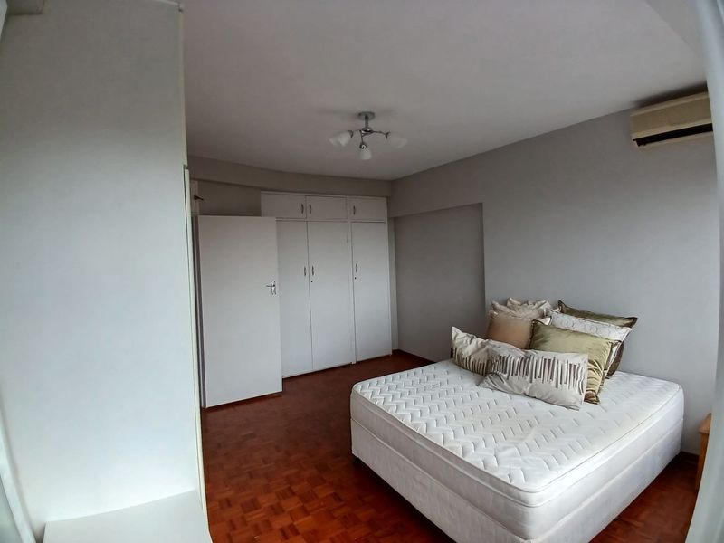 Spacious bedroom featuring classic parquet flooring, ample built-in cupboard storage, and a wall-mounted air conditioning unit for climate control.
