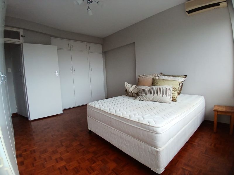 A bedroom featuring parquet flooring, built-in cupboards for storage, and a wall-mounted air conditioning unit.