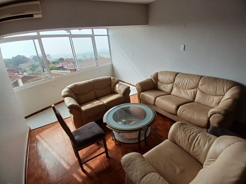 Spacious living room featuring warm parquet flooring, a wall-mounted air conditioning unit, and large windows offering natural light and neighborhood views.