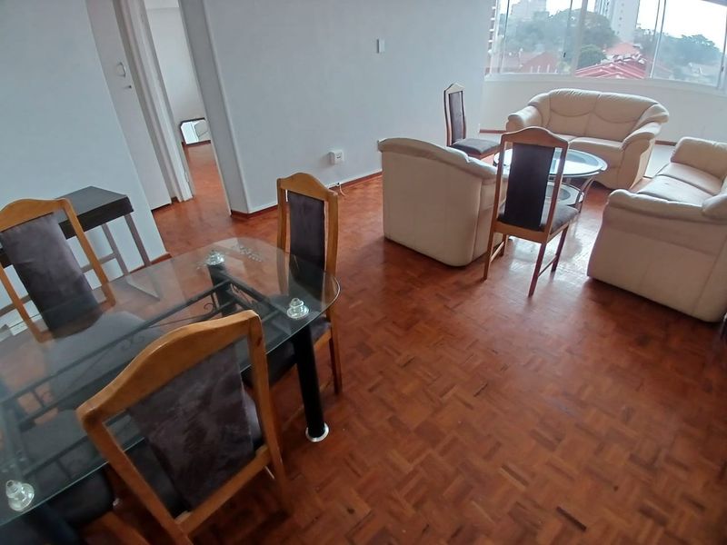Open plan living and dining area featuring classic parquet flooring and large windows providing natural light and urban views.
