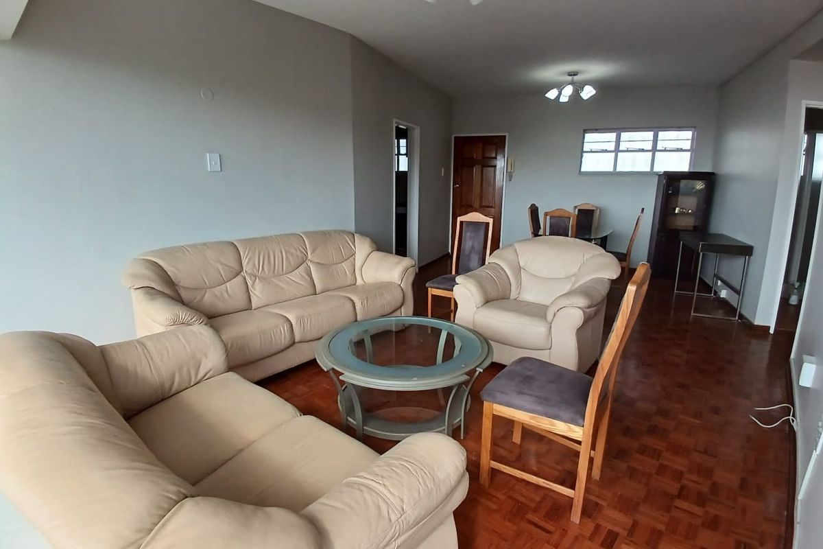 Spacious living area featuring classic parquet flooring, neutral wall tones, and natural light through a multi-pane window.