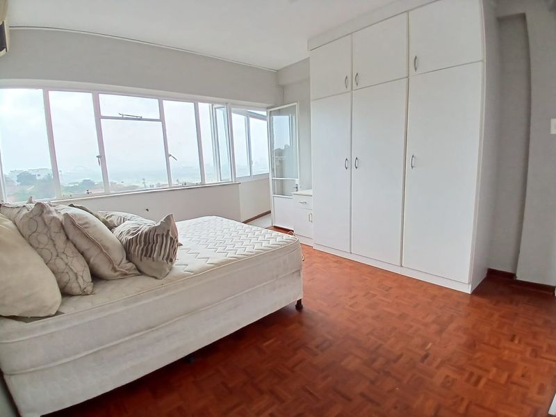 A bedroom featuring parquet flooring, extensive built-in cupboards, and large windows providing natural light and exterior views.