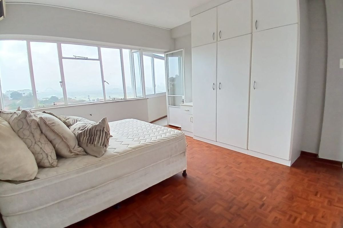 A bedroom featuring parquet flooring, extensive built-in cupboards, and large windows providing natural light and exterior views.