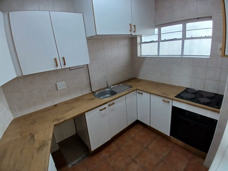 A functional kitchen featuring white cabinetry, wood-look laminate countertops, a built-in oven and hob, and tiled flooring.
