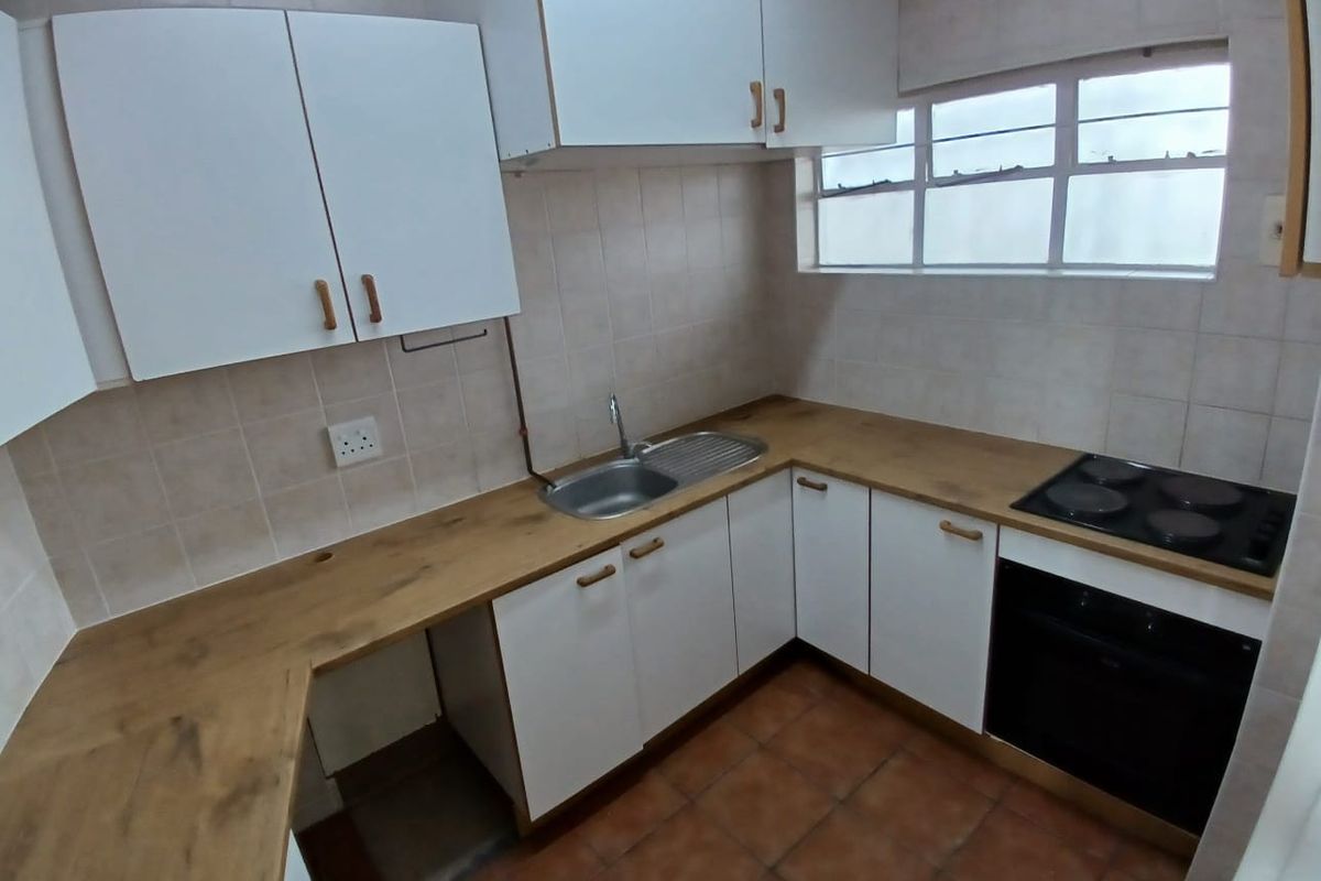 A functional kitchen featuring white cabinetry, wood-look laminate countertops, a built-in oven and hob, and tiled flooring.