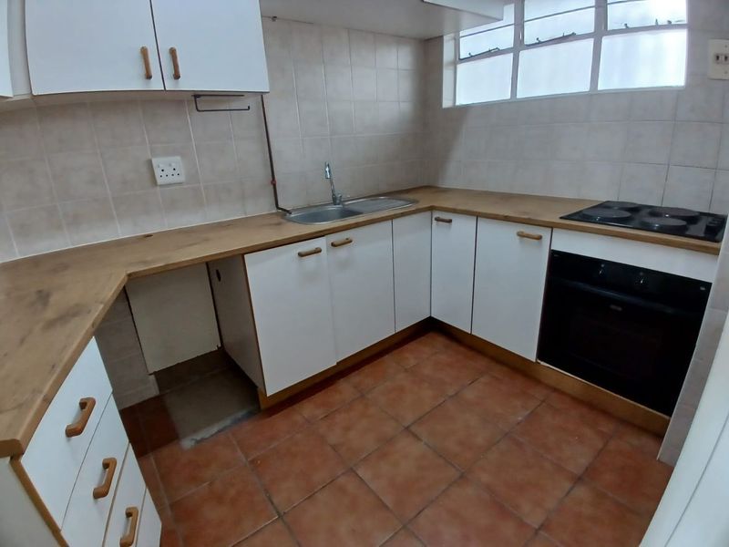 A functional kitchen featuring white cabinetry, wood-look laminate countertops, built-in oven and hob, and tiled flooring, offering a clean space ready for updates.