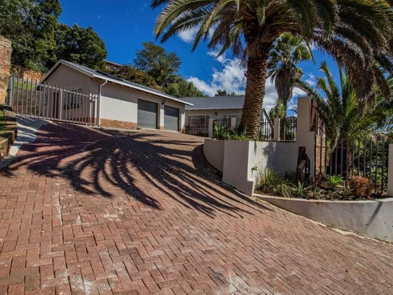 Front exterior view of the property featuring a paved driveway leading to a double garage, complemented by established landscaping and secure perimeter fencing.