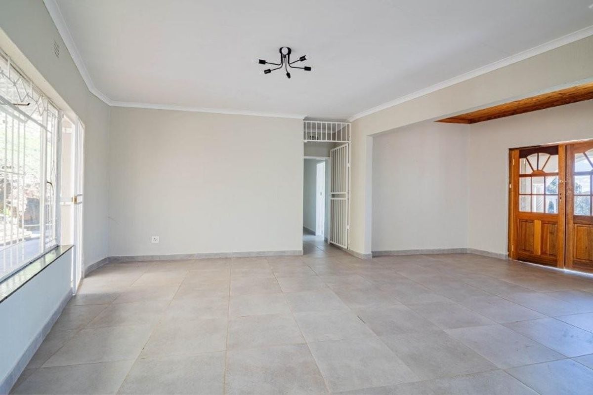 A spacious, empty living area featuring neutral tiled flooring, a security gate, and a wooden door leading to the exterior.