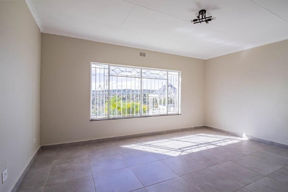 A bright, empty bedroom featuring neutral wall paint, tiled flooring, and a large window with security bars.