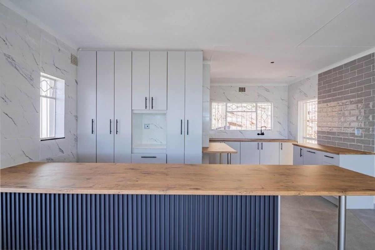 Modern kitchen featuring sleek white cabinetry, timber-look countertops, a breakfast bar, and stylish marble-effect wall tiling with a subway tile backsplash.