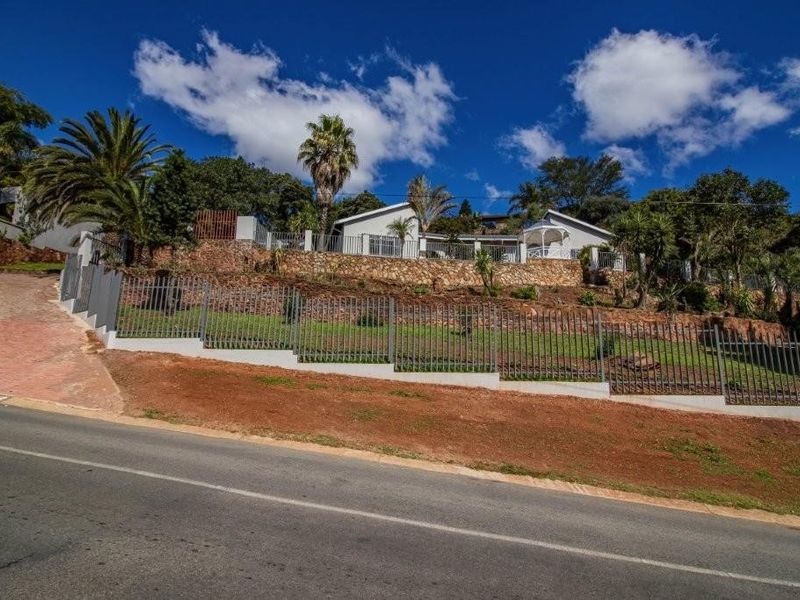 Front elevation of the property featuring a stone retaining wall, metal perimeter fencing, and a landscaped garden area viewed from the street.