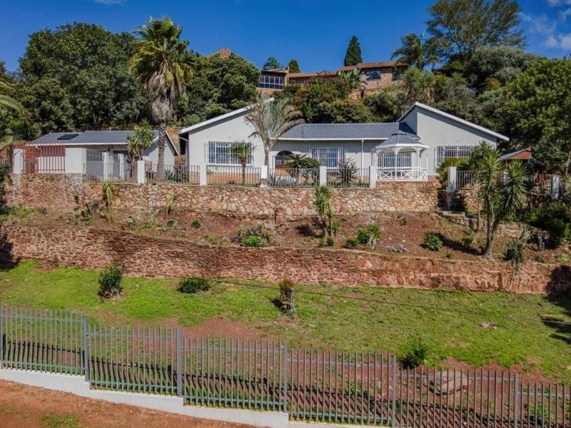 Elevated front view of a residential property featuring tiered stone retaining walls, metal perimeter fencing, and a landscaped garden area.