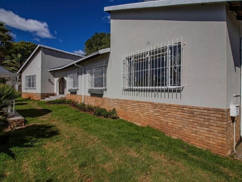 A view of the rear exterior of the house featuring a brick plinth, security bars on windows, and a well-maintained lawn.