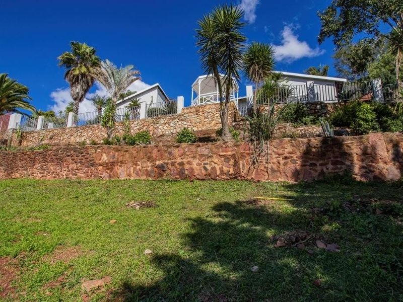A rear view of the property featuring tiered stone retaining walls, established garden landscaping, and an elevated gazebo structure.