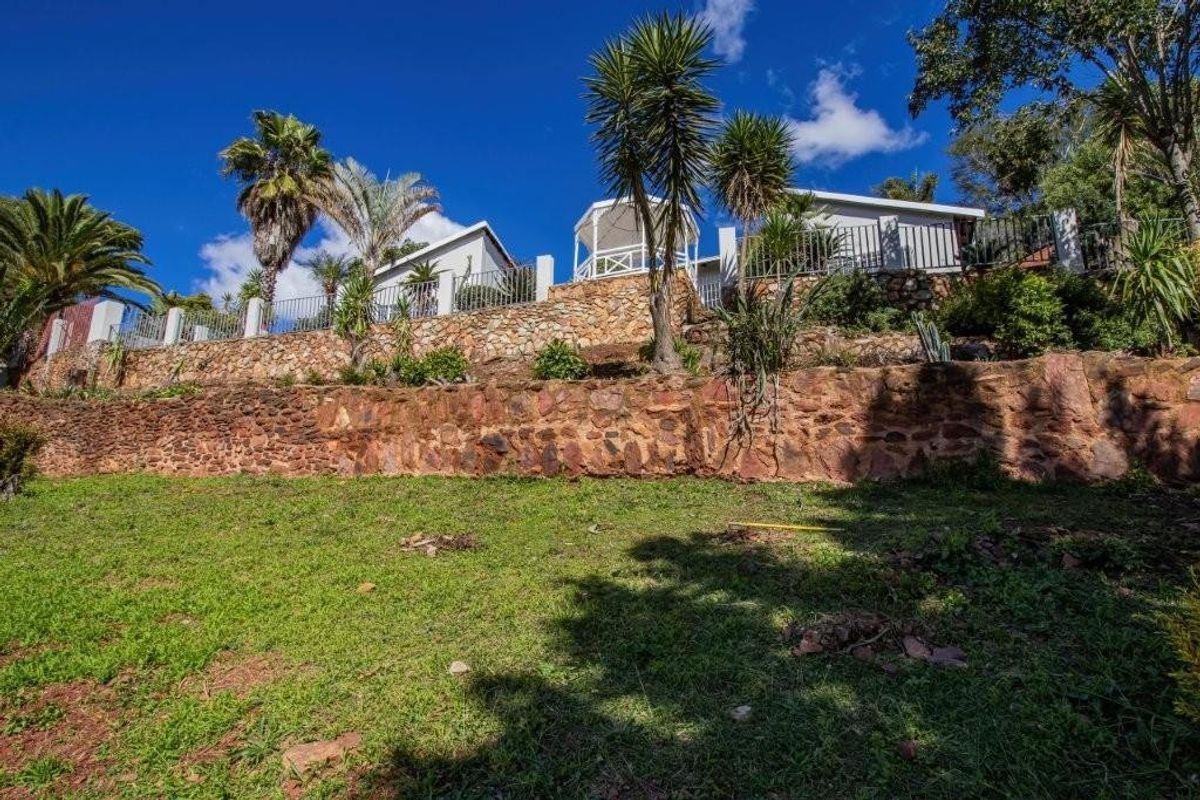 A rear view of the property featuring tiered stone retaining walls, established garden landscaping, and an elevated gazebo structure.