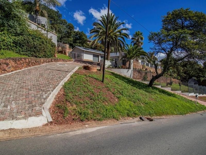 A view of the property frontage featuring a cobblestone driveway, stone retaining walls, and established landscaping leading up to the residence.