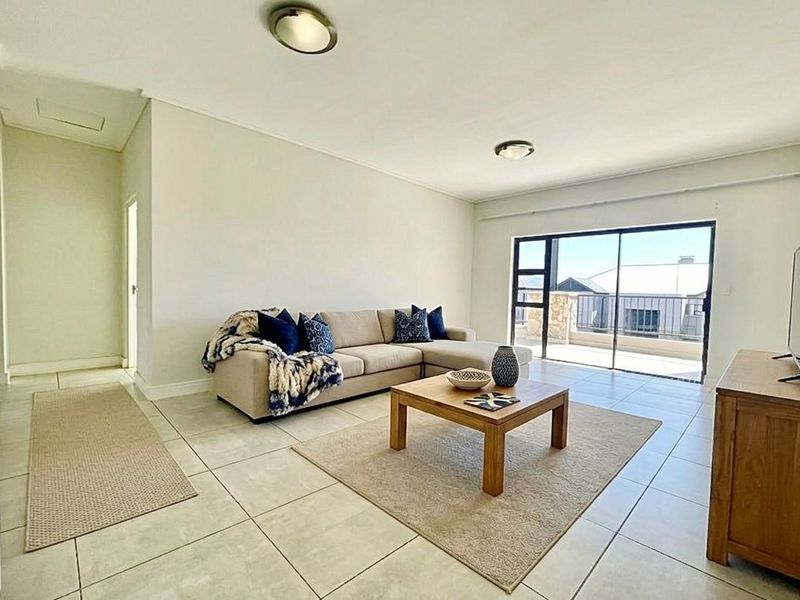 A bright and spacious living room featuring neutral tiled flooring and a large sliding glass door providing access to an outdoor balcony area.