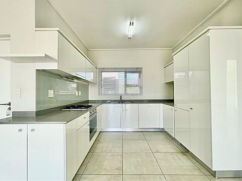 Modern kitchen featuring white high-gloss cabinetry, stone countertops, integrated oven, gas hob, and tiled flooring in a clean, minimalist layout.