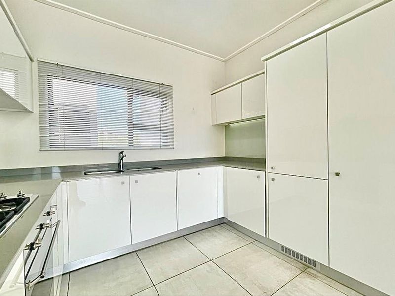 A clean, modern kitchen featuring white high-gloss cabinetry, integrated appliances, a gas hob, and neutral tiled flooring.
