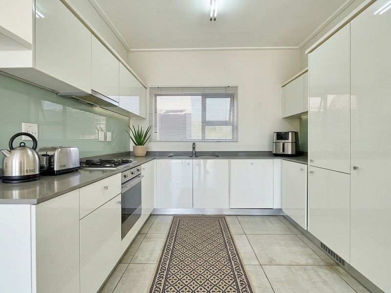 Modern U-shaped kitchen featuring high-gloss white cabinetry, stone countertops, integrated appliances, and a sleek glass splashback.