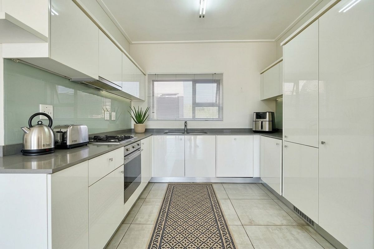 Modern U-shaped kitchen featuring high-gloss white cabinetry, stone countertops, integrated appliances, and a sleek glass splashback.