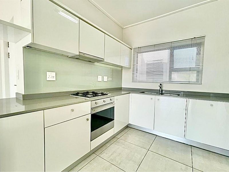 Modern kitchen featuring glossy white cabinetry, stone countertops, integrated gas hob, built-in oven, and a glass splashback with tiled flooring.