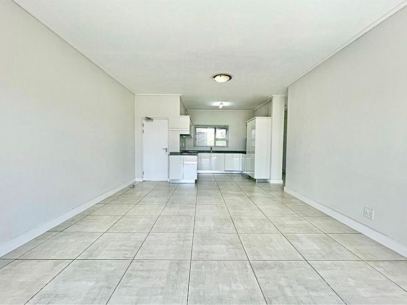 An open-plan living and kitchen area featuring neutral tiled flooring, clean white walls, and functional built-in kitchen cabinetry with integrated appliances.