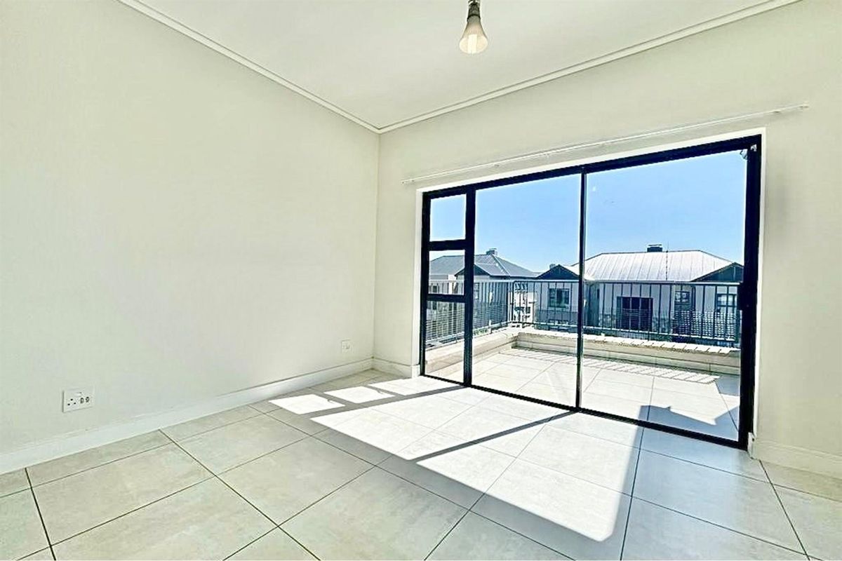 A bright, empty bedroom featuring neutral tiled flooring and large sliding glass doors that open onto a private balcony.