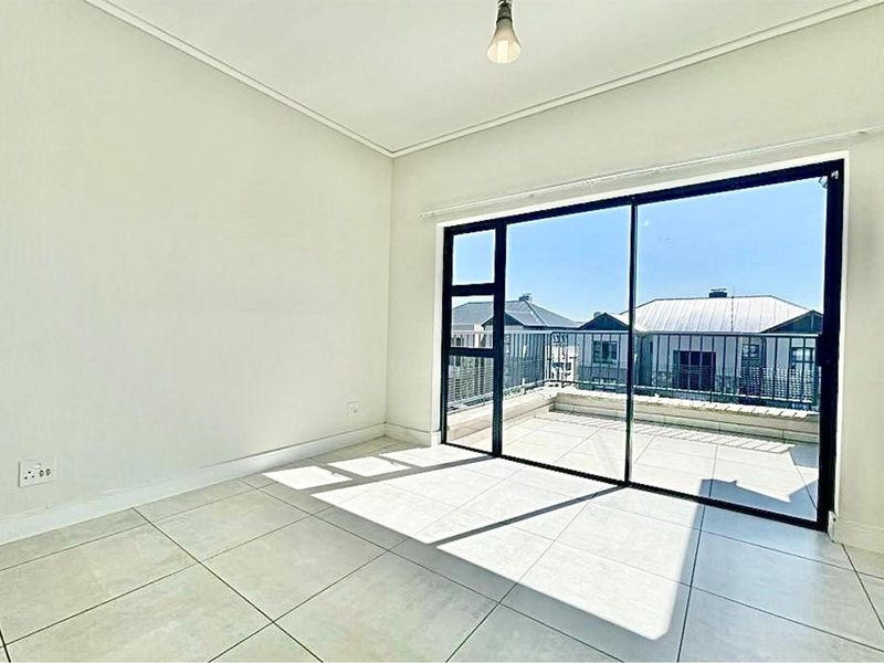 A bright, empty bedroom featuring neutral tiled flooring and large sliding glass doors that open onto a private balcony.