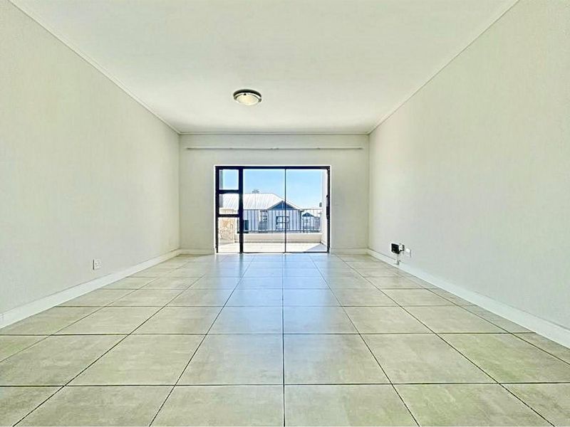 A bright, empty living room featuring neutral tiled flooring and a large sliding glass door providing access to an outdoor area.