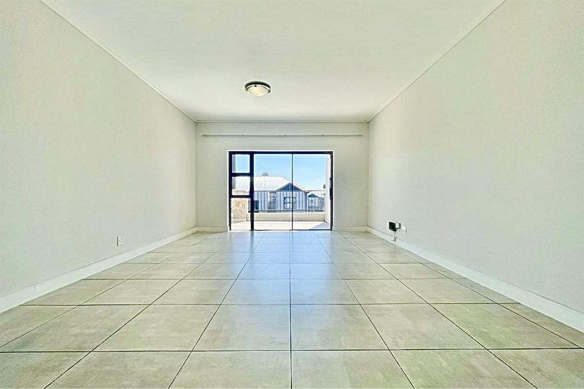 A bright, empty living room featuring neutral tiled flooring and a large sliding glass door providing access to an outdoor area.