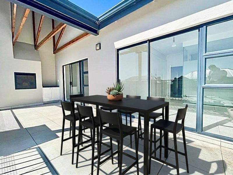 A spacious covered patio featuring exposed timber rafters, a built-in braai, and large sliding glass doors providing seamless indoor-outdoor flow.