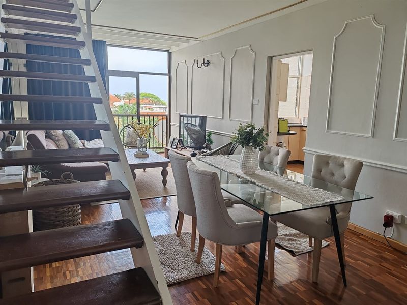 Open plan living and dining area featuring parquet flooring, decorative wall molding, and a wooden staircase leading to an upper level with balcony access.