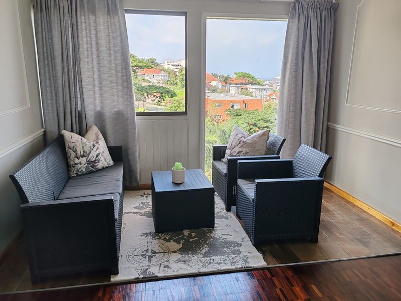 A bright living area featuring polished timber flooring, classic wainscoting, and large windows offering pleasant neighborhood views.