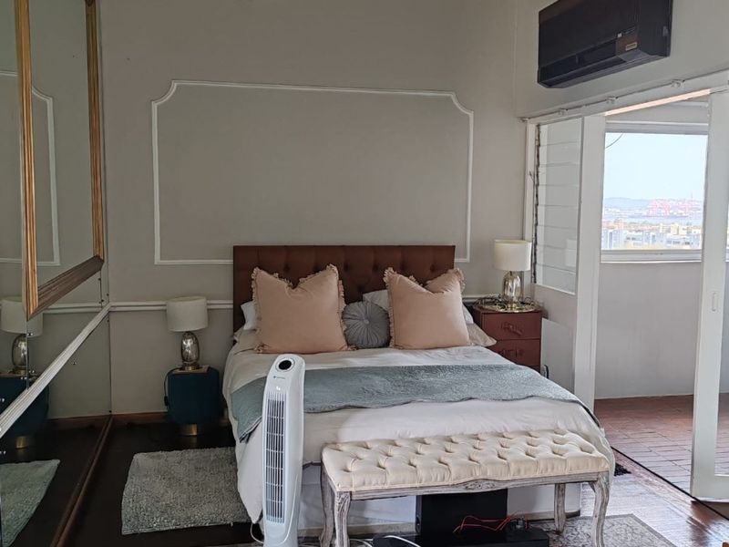 A bedroom featuring exposed ceiling beams, timber flooring, a wall-mounted air conditioning unit, and direct access to an outdoor balcony area.