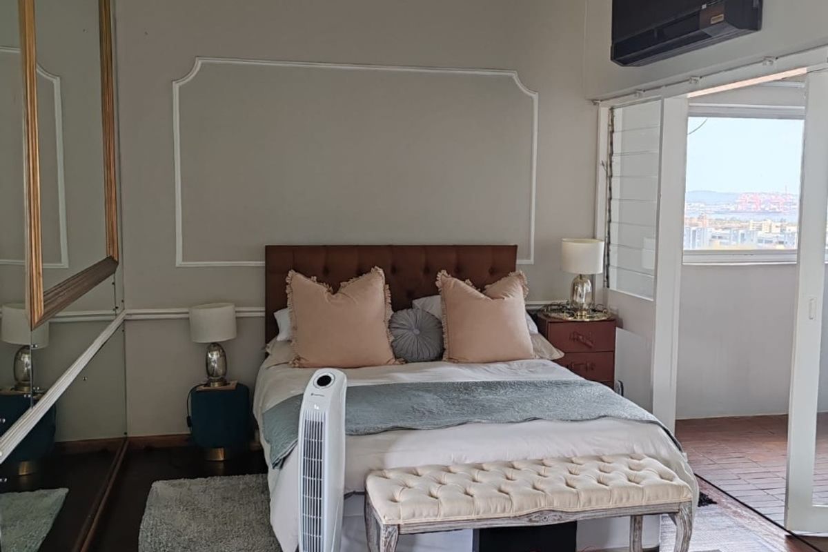 A bedroom featuring exposed ceiling beams, timber flooring, a wall-mounted air conditioning unit, and direct access to an outdoor balcony area.
