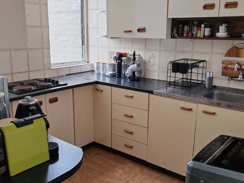 A functional kitchen featuring dated cabinetry, laminate countertops, an electric hob, and ceramic tiling throughout.