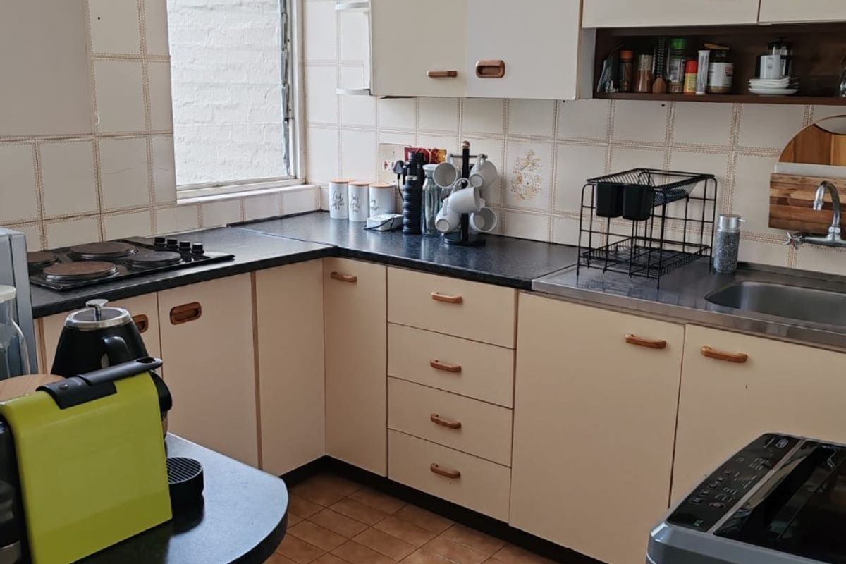 A functional kitchen featuring dated cabinetry, laminate countertops, an electric hob, and ceramic tiling throughout.