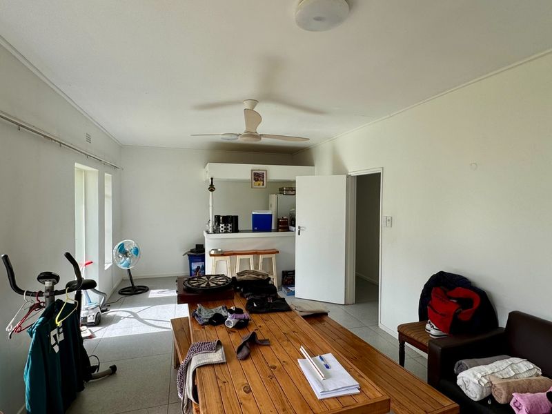 Open plan living area featuring tiled flooring, a ceiling fan, and a built-in bar counter, offering a versatile space for relaxation and entertaining.