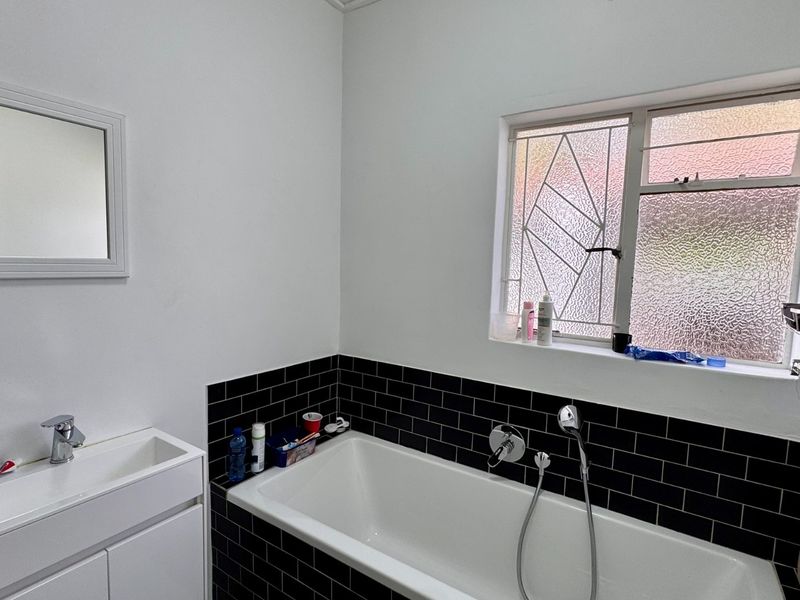 A clean bathroom featuring a white bathtub with black subway tile surround, a modern vanity basin, and a decorative leaded glass window.