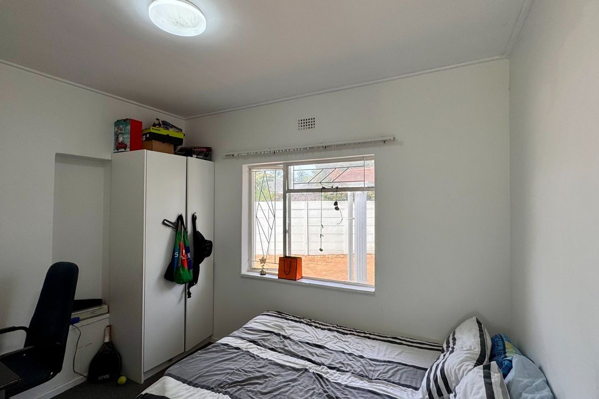 A standard bedroom featuring a window with a curtain track and a built-in ventilation grille.