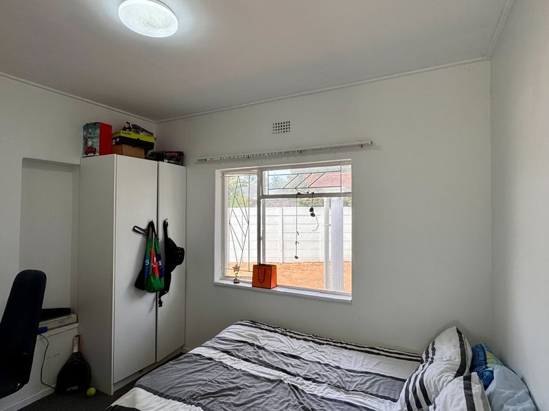 A standard bedroom featuring a window with a curtain track and a built-in ventilation grille.