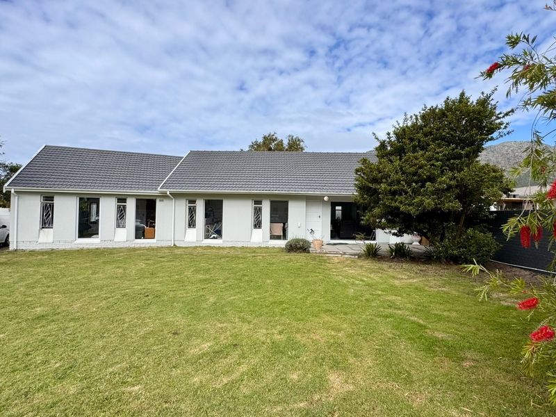 A rear view of the house featuring a tiled roof, security-barred windows, a paved patio area, and a spacious lawn.