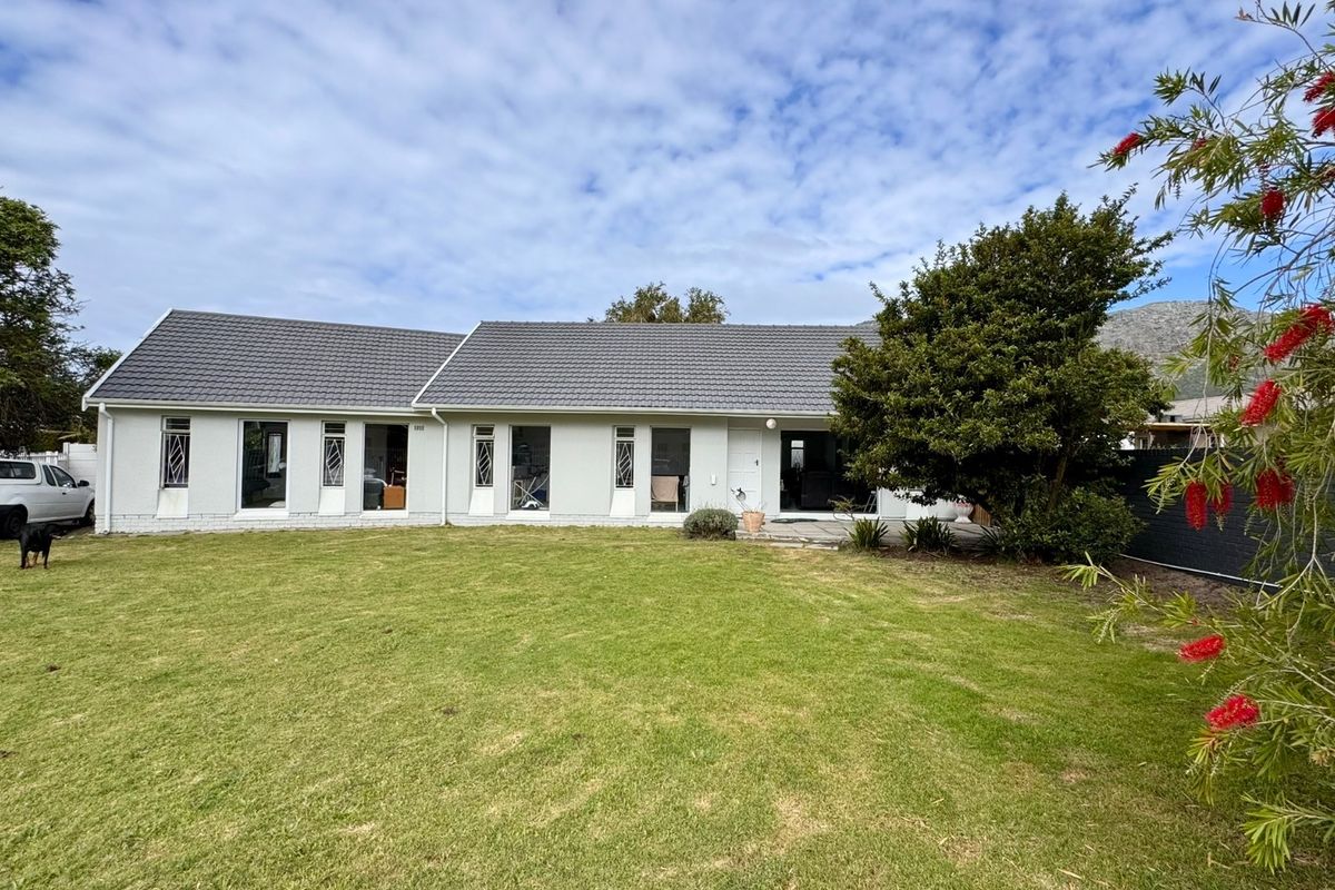 A rear view of the house featuring a tiled roof, security-barred windows, a paved patio area, and a spacious lawn.