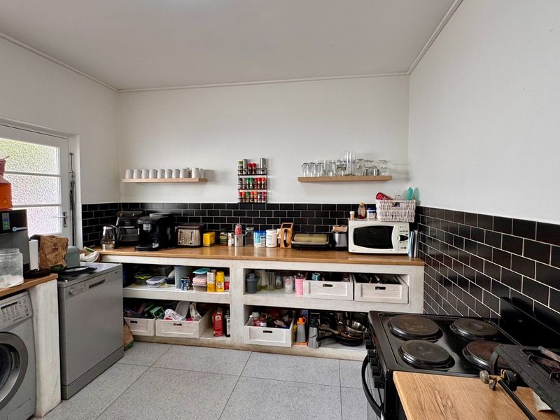 A functional kitchen featuring black subway tile backsplash, wooden countertops, open concrete shelving, and a built-in electric stove with integrated laundry appliances.