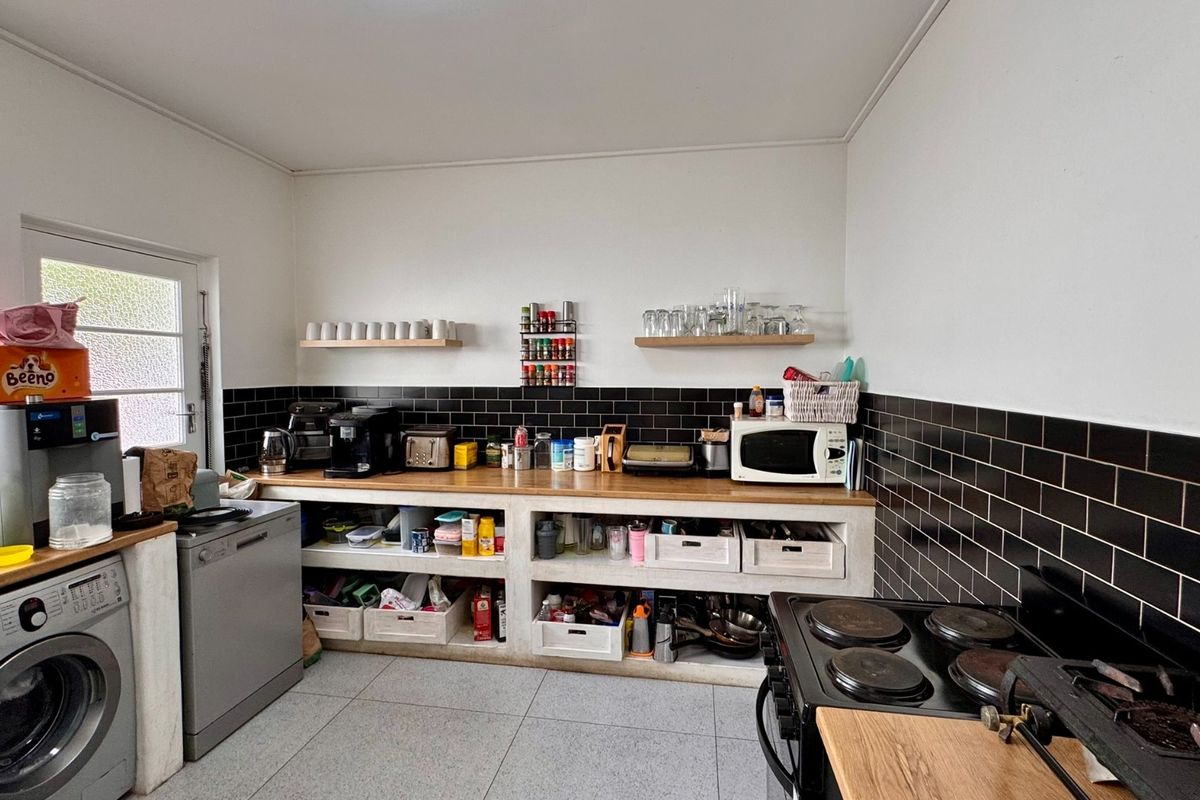 A functional kitchen featuring black subway tile backsplash, wooden countertops, open concrete shelving, and a built-in electric stove with integrated laundry appliances.