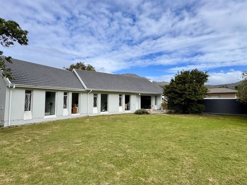A view of the rear elevation of the house featuring a tiled roof, large windows with security bars, and a spacious private lawn.
