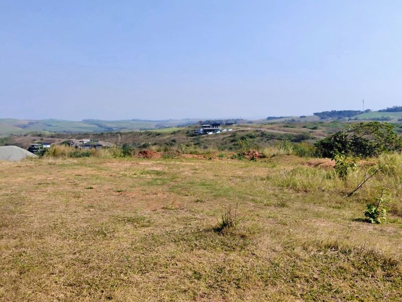 A wide-angle view of the vacant residential land, showcasing the natural landscape and surrounding hilly terrain.