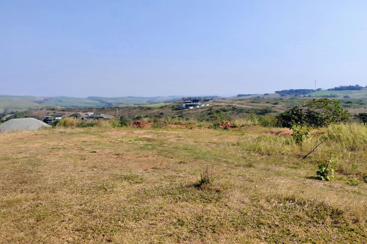 A wide-angle view of the vacant residential land, showcasing the natural landscape and surrounding hilly terrain.