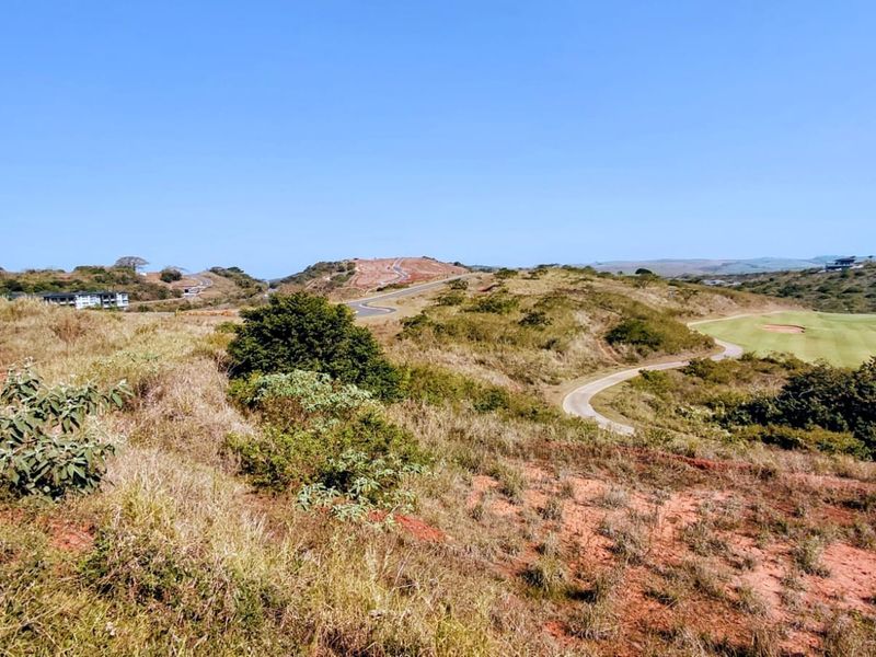 A scenic view of the surrounding landscape, featuring rolling hills, natural vegetation, a paved road, and a portion of a golf course.